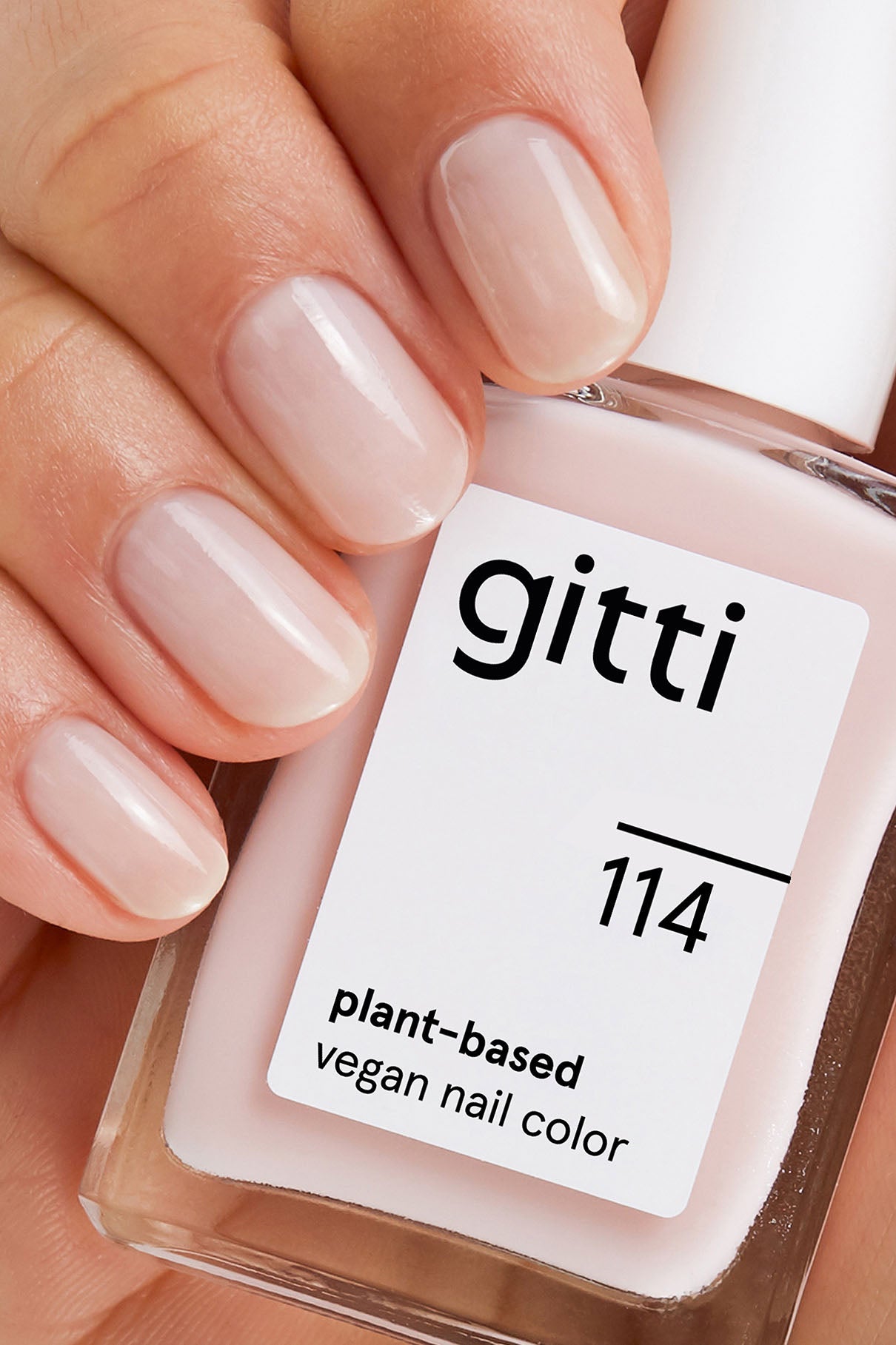 Eine Hand mit kurzen, gepflegten Nägeln, die in leichtem Blassrosa lackiert sind, hält eine Flasche aus dem Express-All-in-One-Set mit der Bezeichnung 114, die mit High Gloss Top Coat für zusätzlichen Glanz versehen ist.