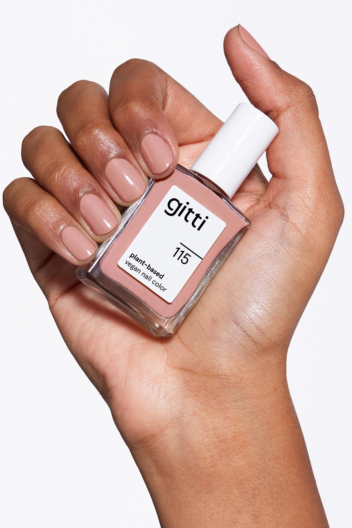 Eine Hand mit kurzen, sauber manikürten Nägeln, die in einem hellen Beige-Braun-Ton lackiert sind, hält ein Fläschchen mit gitti no. 115 vegane Nagelfarbe auf Pflanzenbasis.
