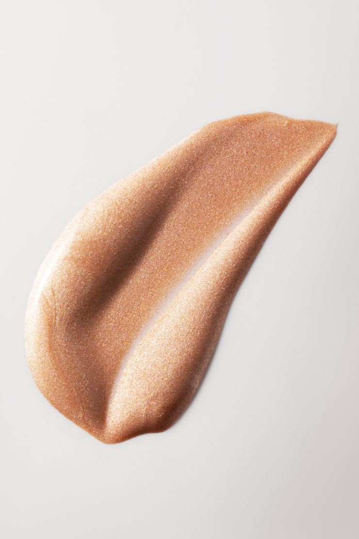 Ein Klecks All Glow, ein bronzefarben schimmernder flüssiger oder multifunktionaler Highlighter, auf eine helle Fläche.