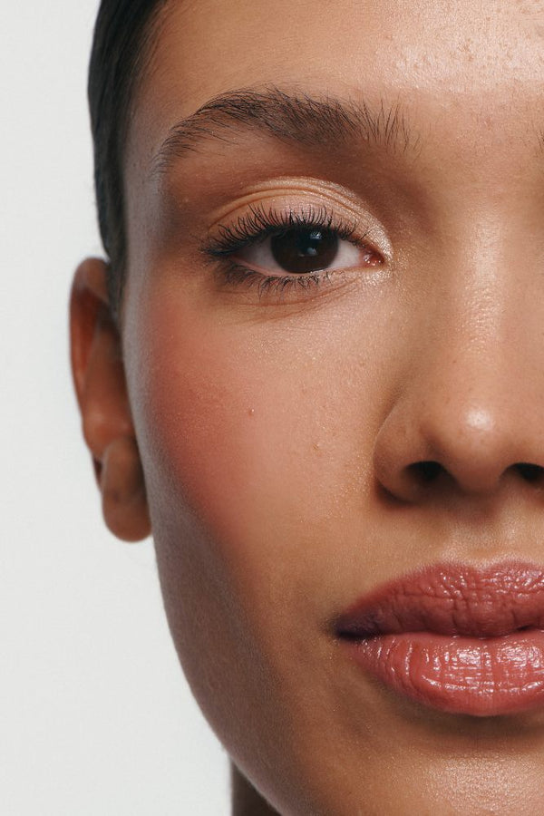 Nahaufnahme eines Frauengesichts mit klarer Haut, natürlichem Make-up und definierten Wimpern, die durch Lash Duo Mascara betont werden, vor einem unifarbenen Hintergrund.