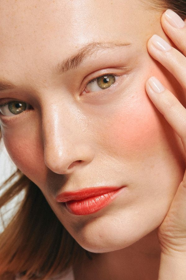 Nahaufnahme des Gesichts einer Person mit neutralem Make-up, Velvet Cheeks Rouge auf den Wangen, hellrosa Nägeln und Fingern, die auf der Wange ruhen - perfekt abgestimmt mit unserem Lip & Cheek Duo.