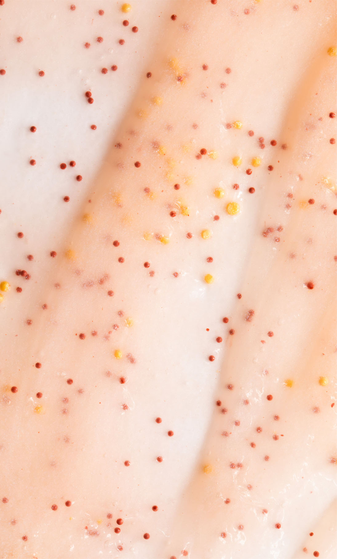 Nahaufnahme des AHA Jelly Hand Exfoliator: eine cremige, blassrosa Formel mit roten und gelben Peelingperlen und einem gleichmäßig verteilten AHA-Komplex.