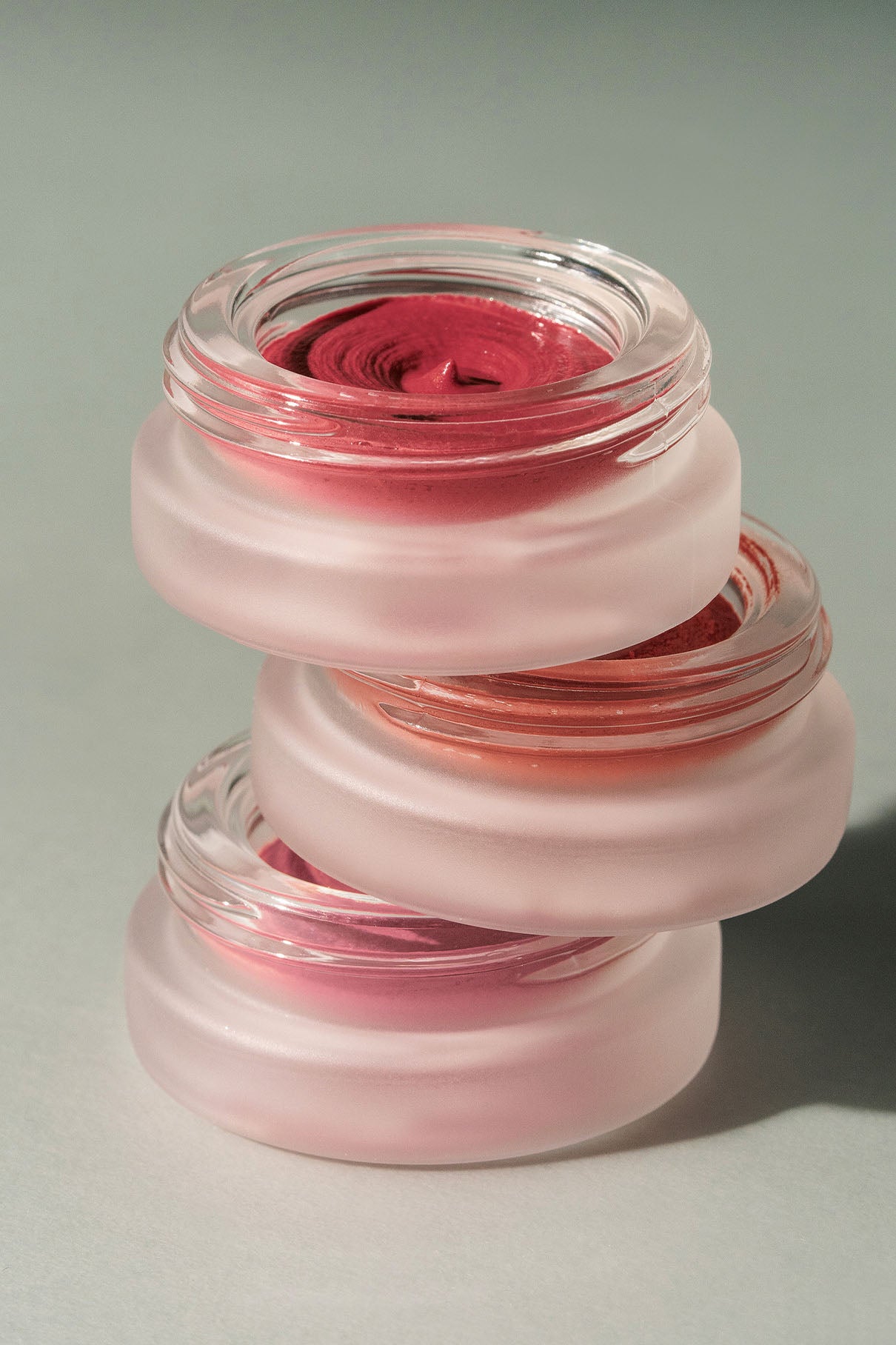 Drei runde Glasbehälter aus dem Signature Set, gefüllt mit verschiedenen Schattierungen von Lip Glaze und Velvet Cheeks Creme Make-up, sind vor einem neutralen Hintergrund übereinander gestapelt.