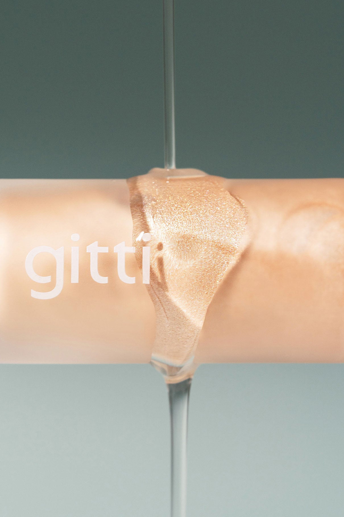 Eine klare Flüssigkeit wird über eine beigefarbene Tube mit der Aufschrift gitti gegossen, die möglicherweise ihr Signature Set vor einem gedämpften grünen Hintergrund enthält.