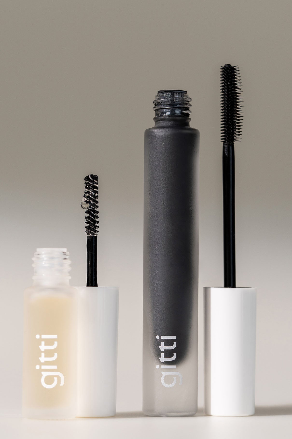 Drei Tuben Brow & Lash Duo in schwarzen und klaren Formeln mit weißen Kappen, zwei davon mit abgenommenen Stiften, um die verschiedenen Pinselformen hervorzuheben.