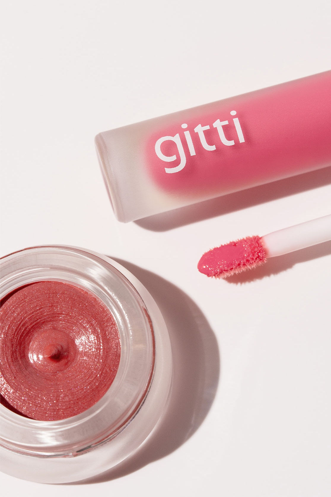 Das Lippen- und Wangen-Duo wird auf einer weißen Fläche mit einer rosafarbenen Tube Lip Glaze und einem geöffneten Tiegel mit schimmerndem, rosafarbenem Velvet Cheeks Creme-Make-up präsentiert.