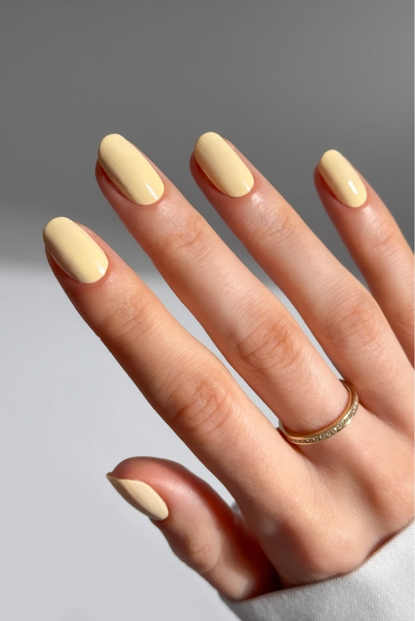 Eine Hand mit kurzen, ovalen Nägeln, die mit Gitti Nr. 032, mit einem dünnen Goldring am Ringfinger vor neutralem Hintergrund.