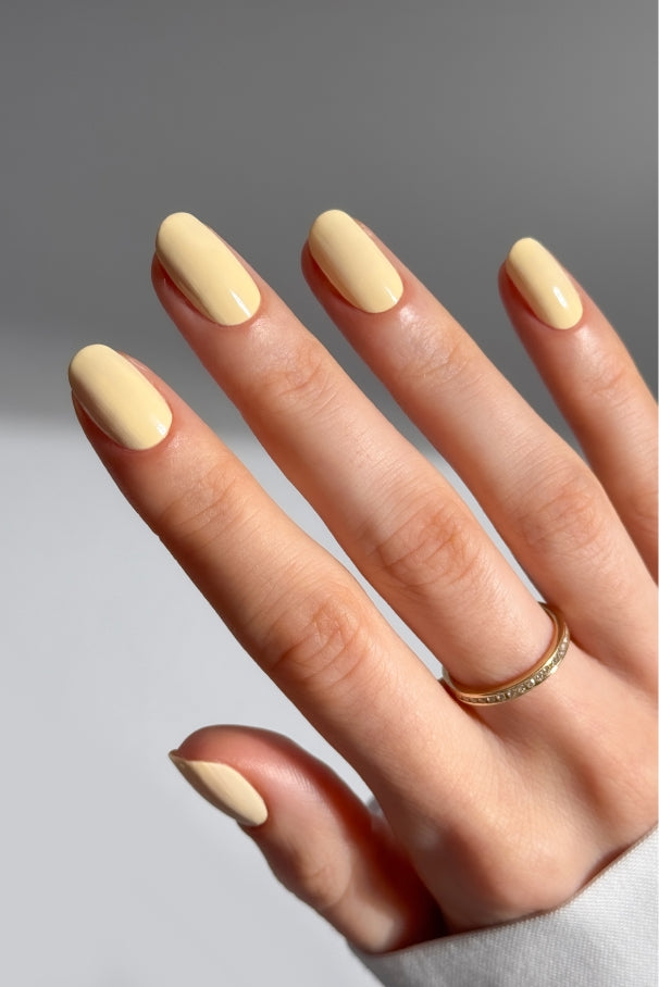 Eine Hand mit kurzen, ovalen Nägeln, die mit Gitti Nr. 032, mit einem dünnen Goldring am Ringfinger vor neutralem Hintergrund.