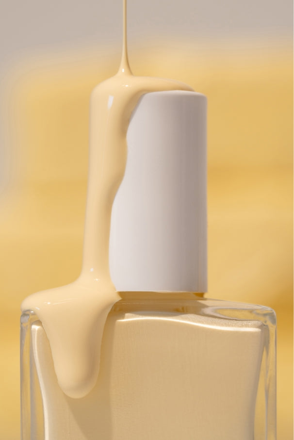 Eine Nahaufnahme einer Klarglas-Nagellackflasche mit der Aufschrift gitti no. 032, mit gelb-weißem Nagellack, der über die weiße Kappe tropft, vor einem gelben Hintergrund.