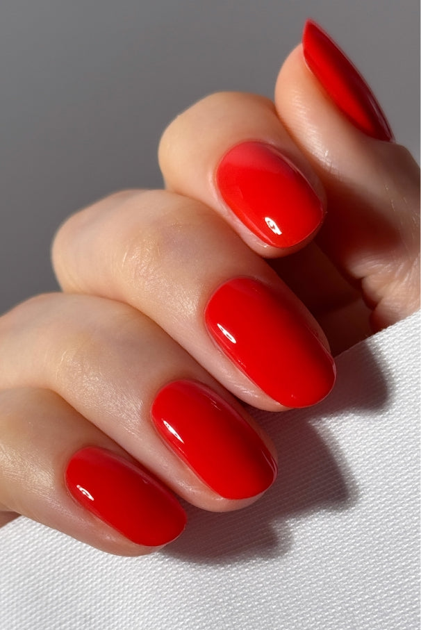 Nahaufnahme einer Hand mit sauber manikürten, in glänzendem, intensivem Tomatenrot (gitti Nr. 033) lackierten Nägeln, die ein Stück weißen Stoff hält.