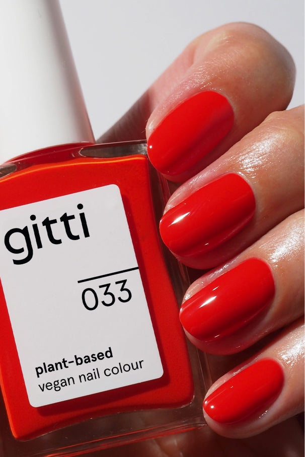 Nahaufnahme einer Hand mit leuchtend rotem Nagellack, die eine Flasche der pflanzlichen veganen Nagelfarbe Quick Dry Routine hält, die mit einem Hochglanz-Top Coat für zusätzlichen Glanz abgeschlossen ist.