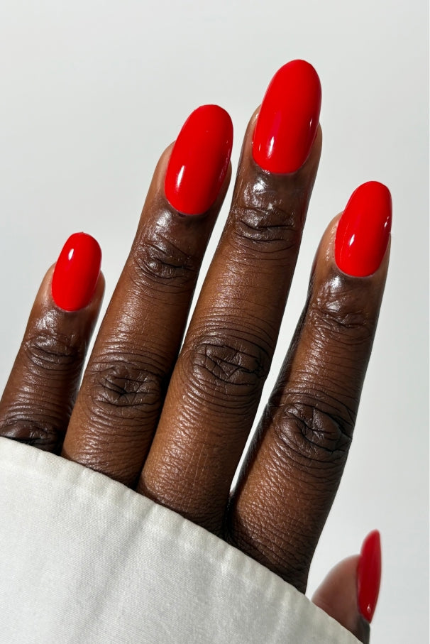 Eine Hand mit dunklem Hautton zeigt sauber manikürte Nägel, die mit gitti no. 033, einem intensiven tomatenroten Nagellack, vor einem schlichten weißen Hintergrund.