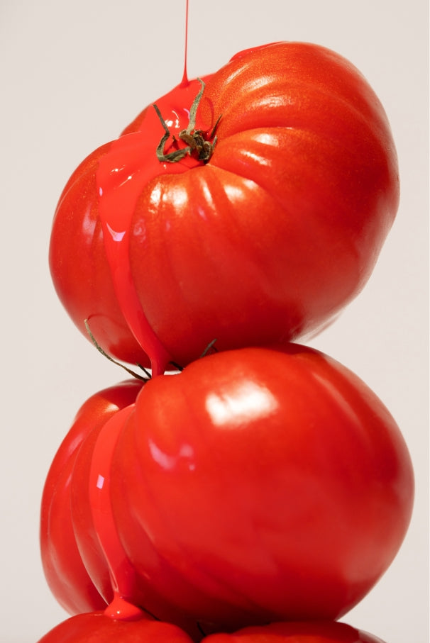Drei reife Tomaten sind gestapelt, über die ein Strom roter Flüssigkeit fließt, um ihr intensives Tomatenrot und ihre glänzende Oberfläche hervorzuheben - genau wie der leuchtende Farbton von gitti no. 033.