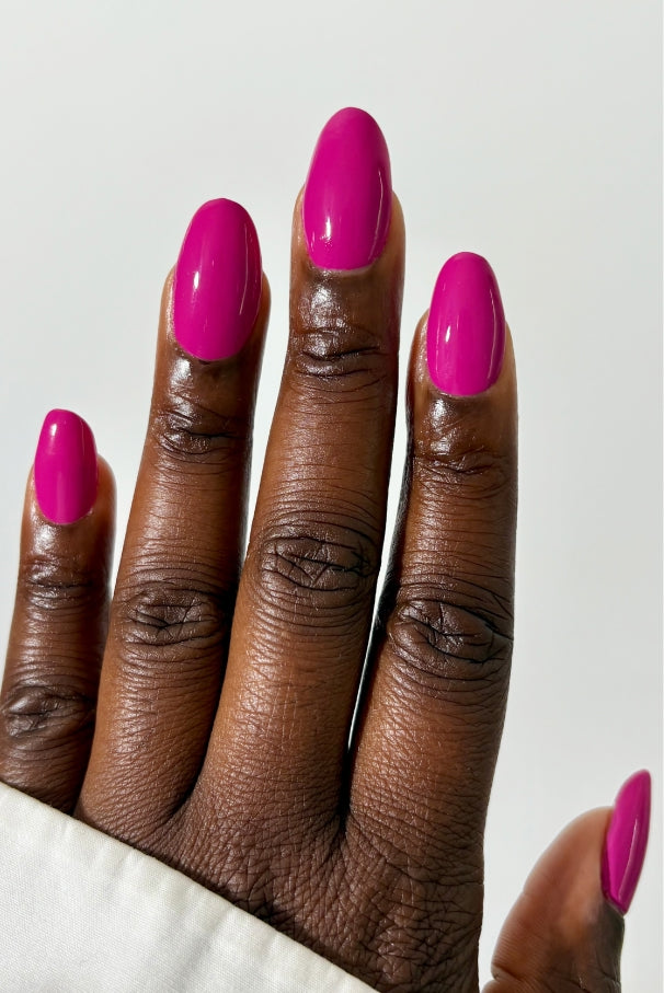 Eine Hand mit dunkler Haut zeigt Fingernägel, die mit gitti no. 034, einer leuchtenden Nagelfarbe in elektrisierendem Fuchsia, vor einem schlichten hellen Hintergrund.