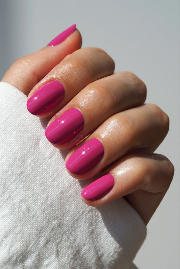 Eine Hand mit sauber manikürten Nägeln, die in gitti no. 034, einem leuchtenden Fuchsia-Ton, der teilweise von einem weißen Ärmel verdeckt wird, ist vor einem schlichten Hintergrund zu sehen.