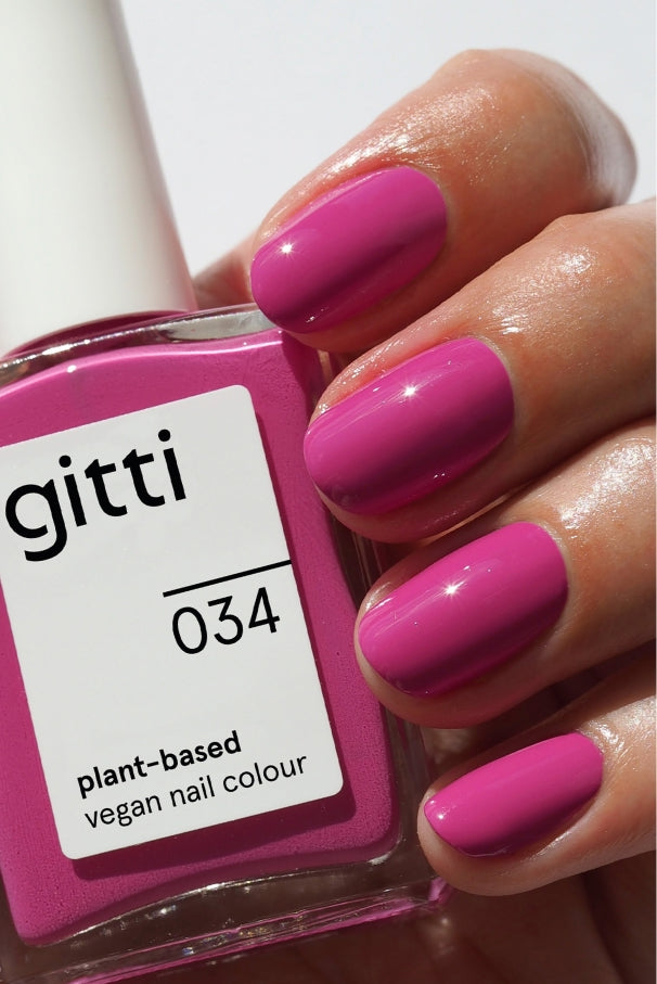 Eine Hand mit sauber manikürten, in leuchtendem Pink lackierten Nägeln hält eine Flasche der pflanzlichen veganen Nagelfarbe Summer Glow Set im gleichen Farbton.