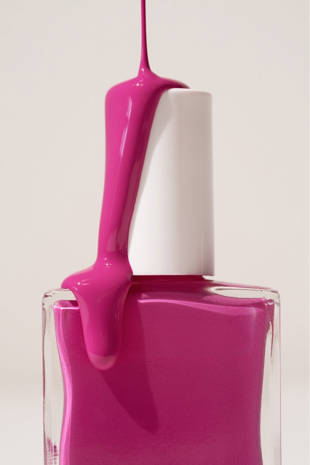 Eine Nahaufnahme einer Flasche Gitti Nr. 034, leuchtende Nagelfarbe in elektrisierendem Fuchsia, mit über die weiße Kappe tropfender Politur vor einfarbigem Hintergrund.