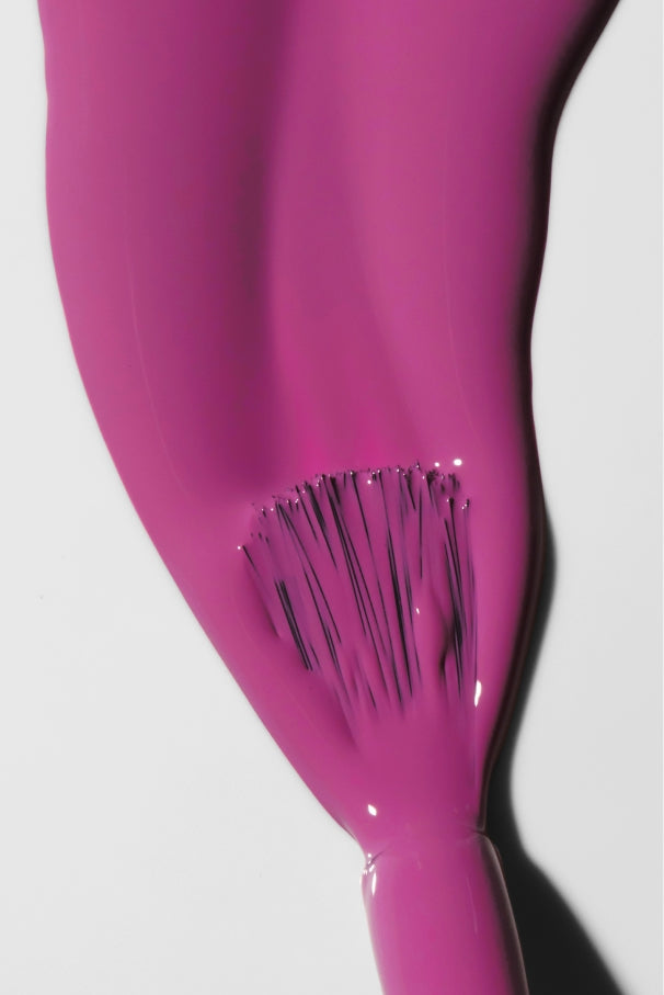 Nahaufnahme eines Pinsels, mit dem eine dicke Schicht von gitti no. 034, einer glänzenden rosafarbenen Nagelfarbe, auf eine weiße Fläche.