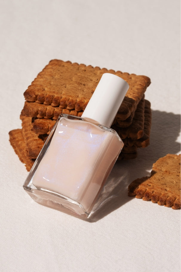 Eine Flasche gitti no. 035, ein zarter Nagellack im semi-transparenten Rosaton mit blauem Schimmer, lehnt an einem Stapel rechteckiger Kekse auf hellem Stoff.