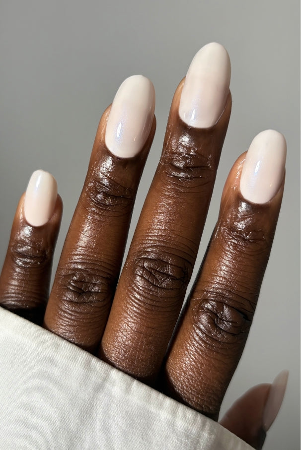 Nahaufnahme einer dunkelhäutigen Hand mit sauber manikürten Nägeln, die mit gitti no. 035, einem halbtransparenten rosafarbenen Nagellack, lackiert sind. Die Person trägt einen hellen Ärmel.