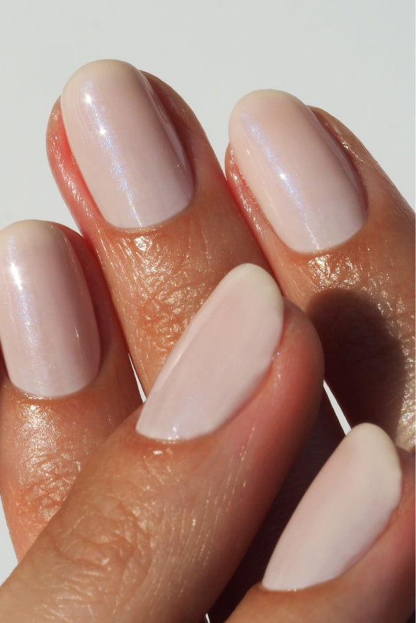 Nahaufnahme einer Hand mit vier sichtbaren Fingern, deren gepflegte Nägel mit einem glänzenden, blassrosa Lack aus dem Set Plant Trio + Remover Balm lackiert sind.
