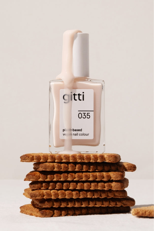 Eine Flasche gitti no. 035 pflanzliche, vegane Nagelfarbe in einem halbtransparenten Rosaton, von dem blasser Lack heruntertropft, steht auf einem Stapel runder Kekse.