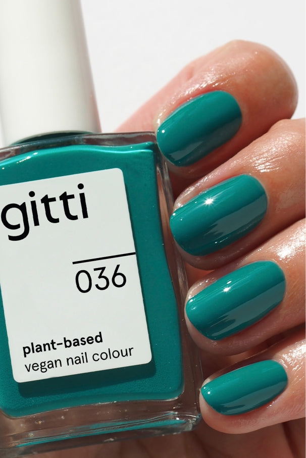 Eine Hand mit blaugrünen Nägeln hält eine Flasche gitti no. 036, eine pflanzliche, vegane Nagelfarbe in mediterranem Grün-Blau, die perfekt zu dem Lack auf den Fingernägeln passt.