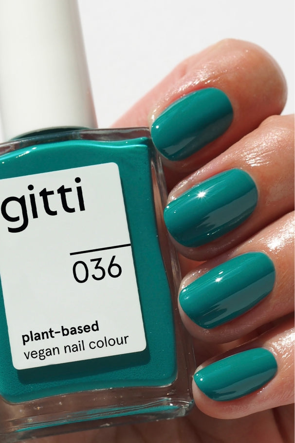 Eine Hand mit blaugrünen Nägeln hält eine Flasche gitti no. 036, eine pflanzliche, vegane Nagelfarbe in mediterranem Grün-Blau, die perfekt zu dem Lack auf den Fingernägeln passt.