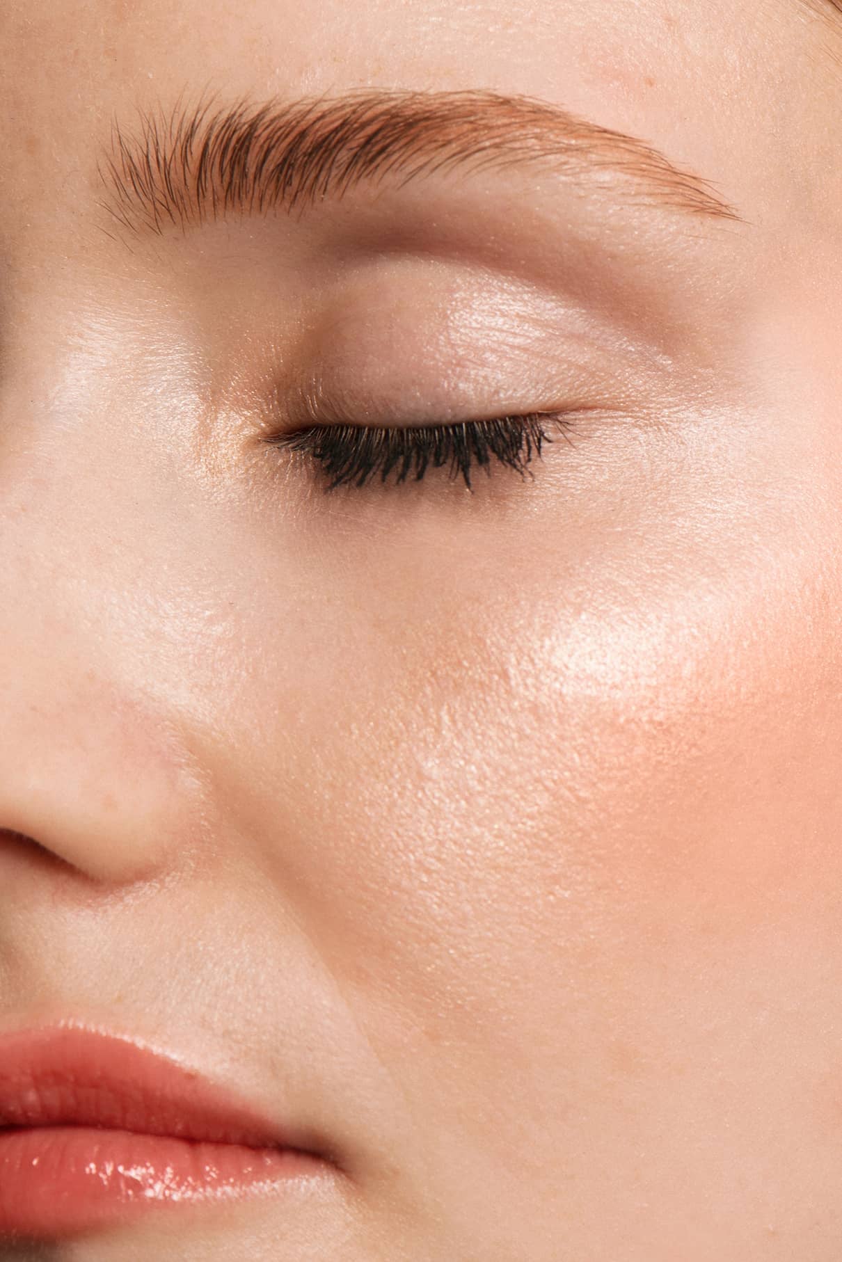 Nahaufnahme des Gesichts einer Person mit geschlossenen Augen, gepflegten Augenbrauen, glatter, strahlender Haut, die durch All Glow Highlighter verstärkt wird, und leicht getönten Lippen.