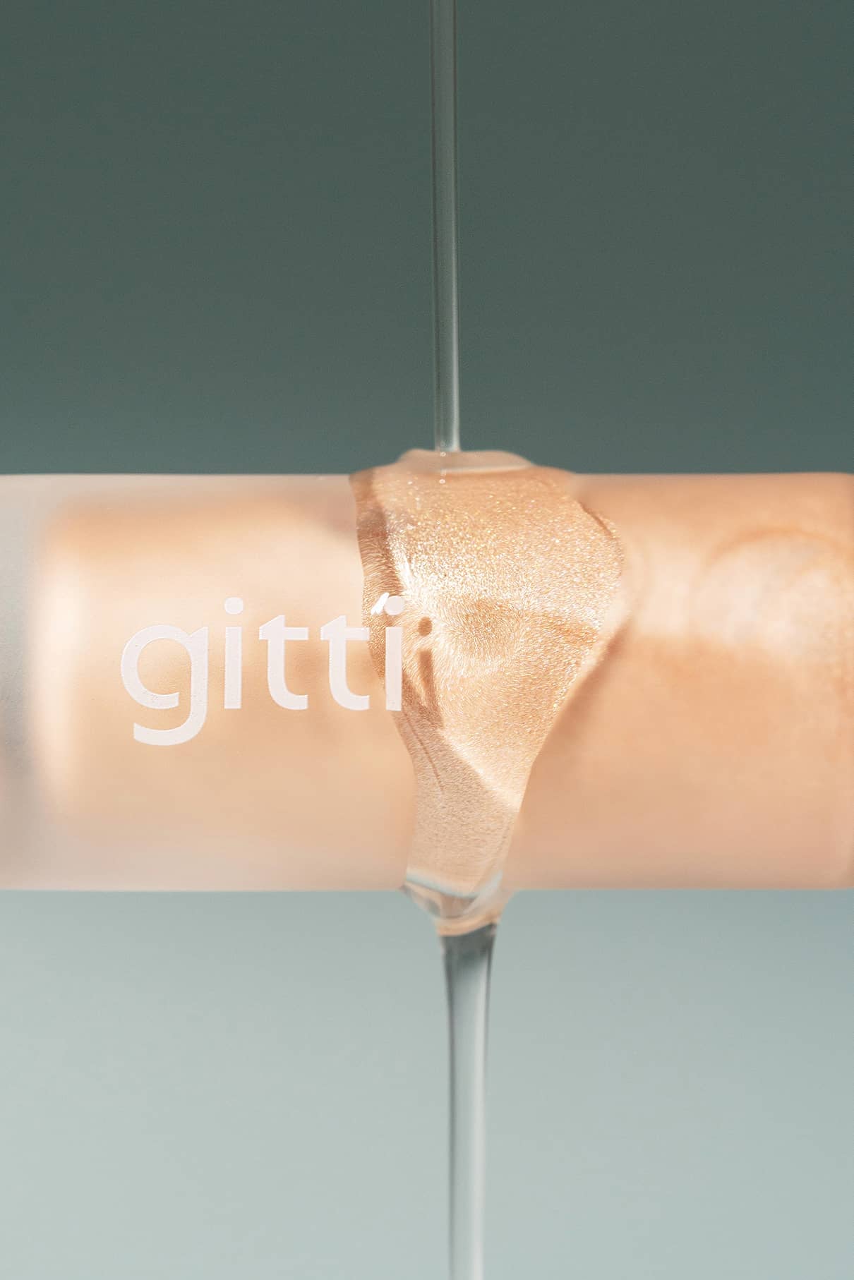 Eine Nahaufnahme der All Glow-Flasche aus Milchglas mit der Aufschrift gitti, die mit beigefarbenem Metallic-Nagellack gefüllt ist und über die sich eine klare Flüssigkeit ergießt, die den leuchtenden Glanz eines flüssigen Highlighters auf den Nägeln widerspiegelt.