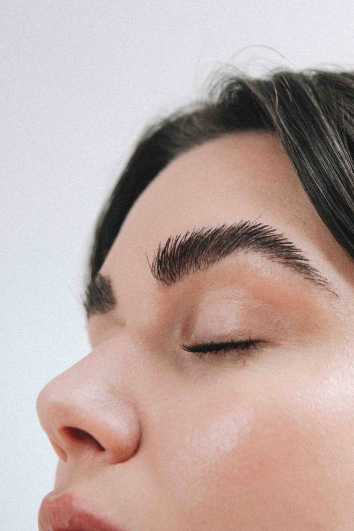 Nahaufnahme des Gesichts einer Person mit geschlossenen Augen, glatter Haut, natürlichem Make-up und gepflegten Augenbrauen, gestylt mit Berlin Brow 02 in Dunkelbraun.