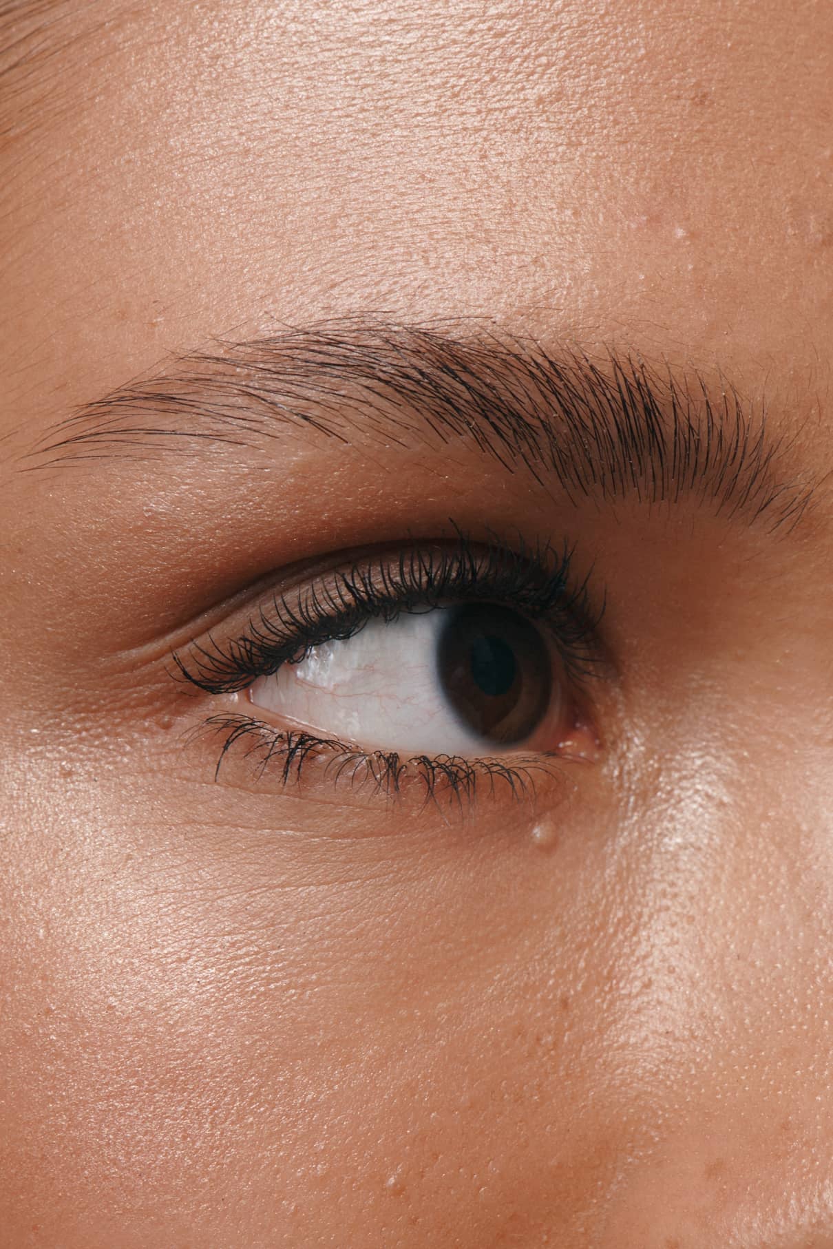 Die Nahaufnahme eines Auges, einer Augenbraue und der oberen Wange zeigt glatte, taufrische Haut - mit perfekt gestylten Augenbrauen unter Verwendung von Brow Control, einem transparenten Augenbrauengel mit einer leichten, nicht klebenden Formel.