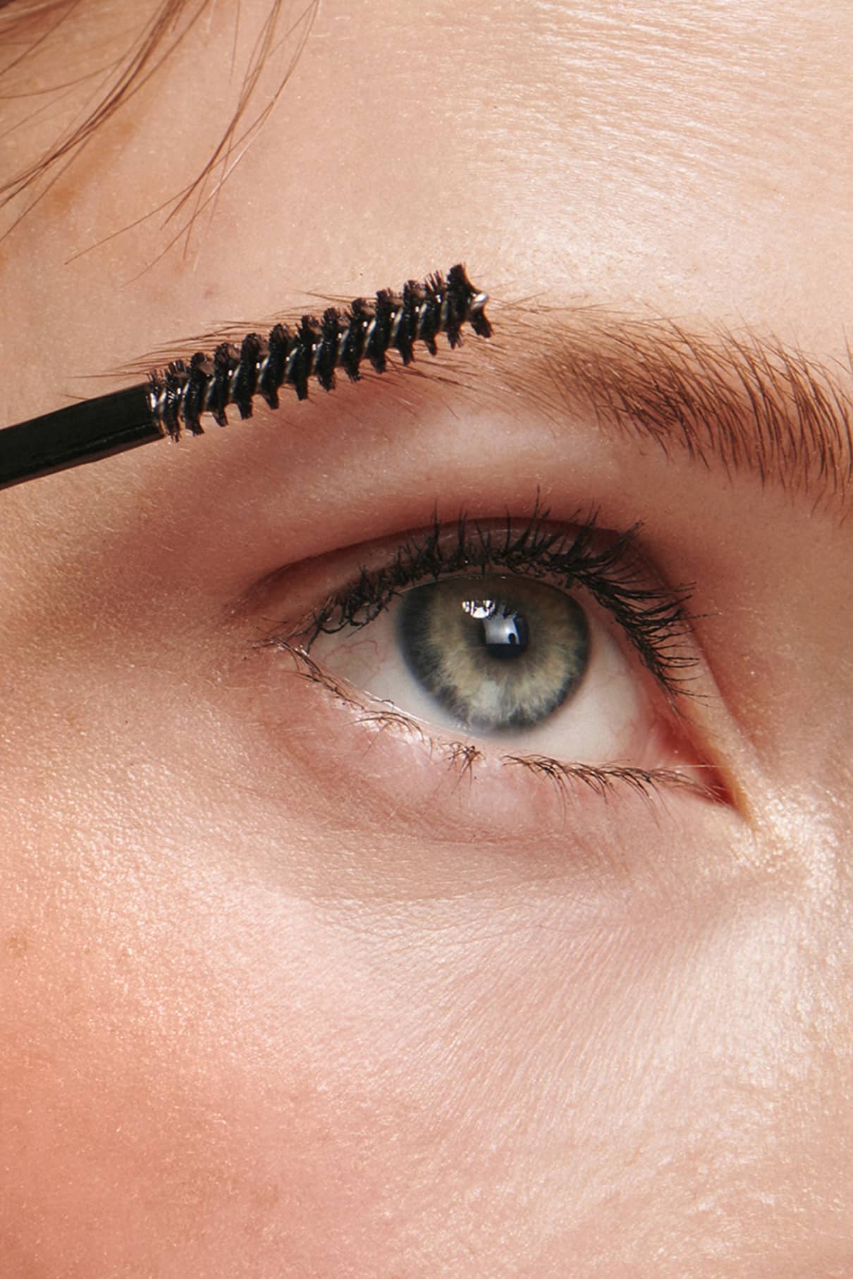 Nahaufnahme einer Person, die Brow Control mit einem Spoolie auf ihre rechte Augenbraue aufträgt, wobei die leichte Textur und das nicht klebende Finish hervorgehoben werden.