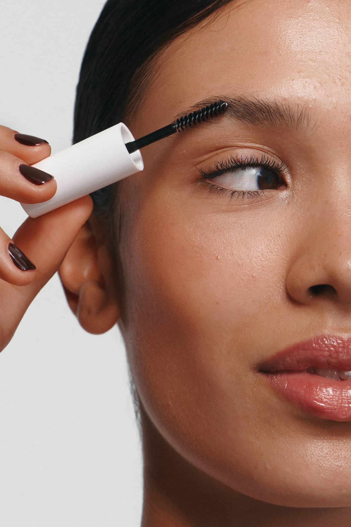 Eine Person verwendet Brow Control mit einem Spoolie-Pinsel, um ihre Augenbraue zu formen. Die Nahaufnahme zeigt nur die Hälfte des Gesichts und hebt die nicht-klebrige, leichte Textur des transparenten Gels hervor.