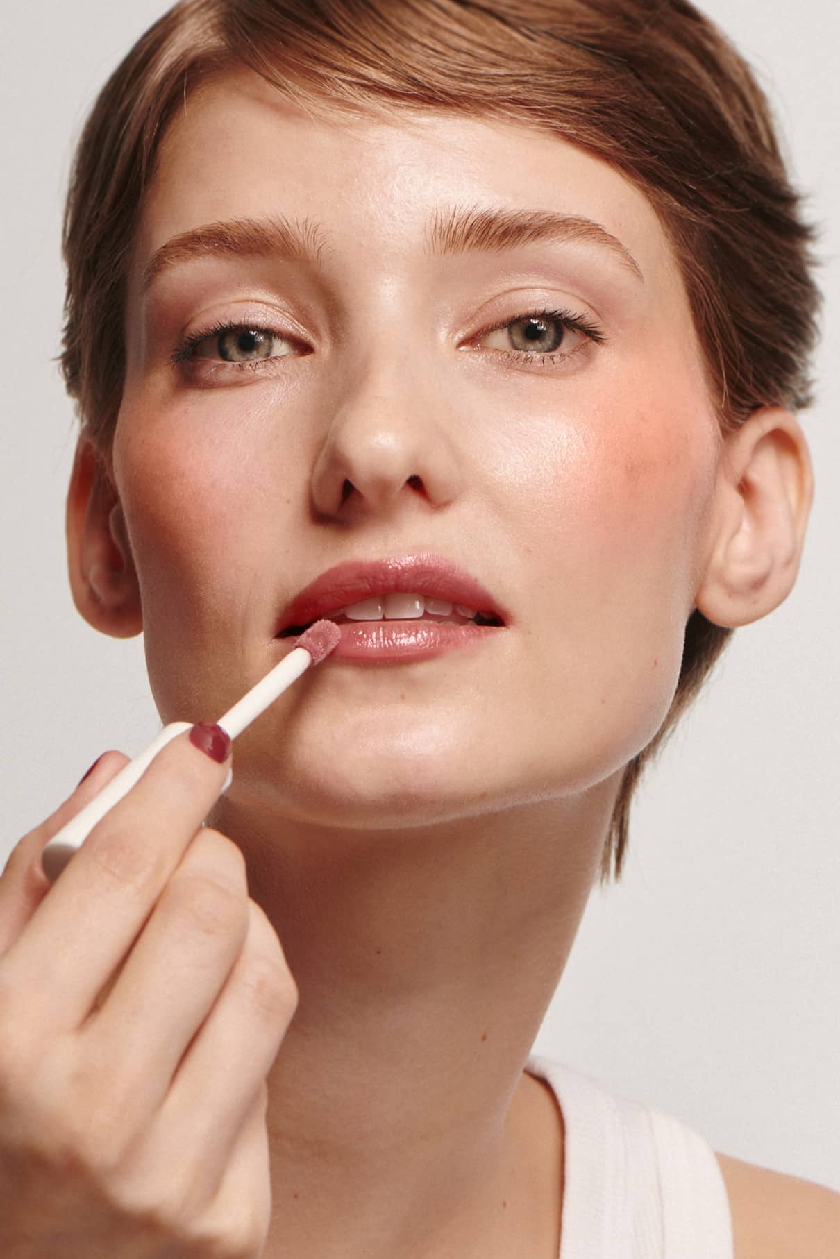 Eine Person mit kurzen Haaren trägt mit einem Zauberstab Lip Glaze no. 01 auf und verleiht ihren Lippen ein rosa, hochglänzendes Finish.