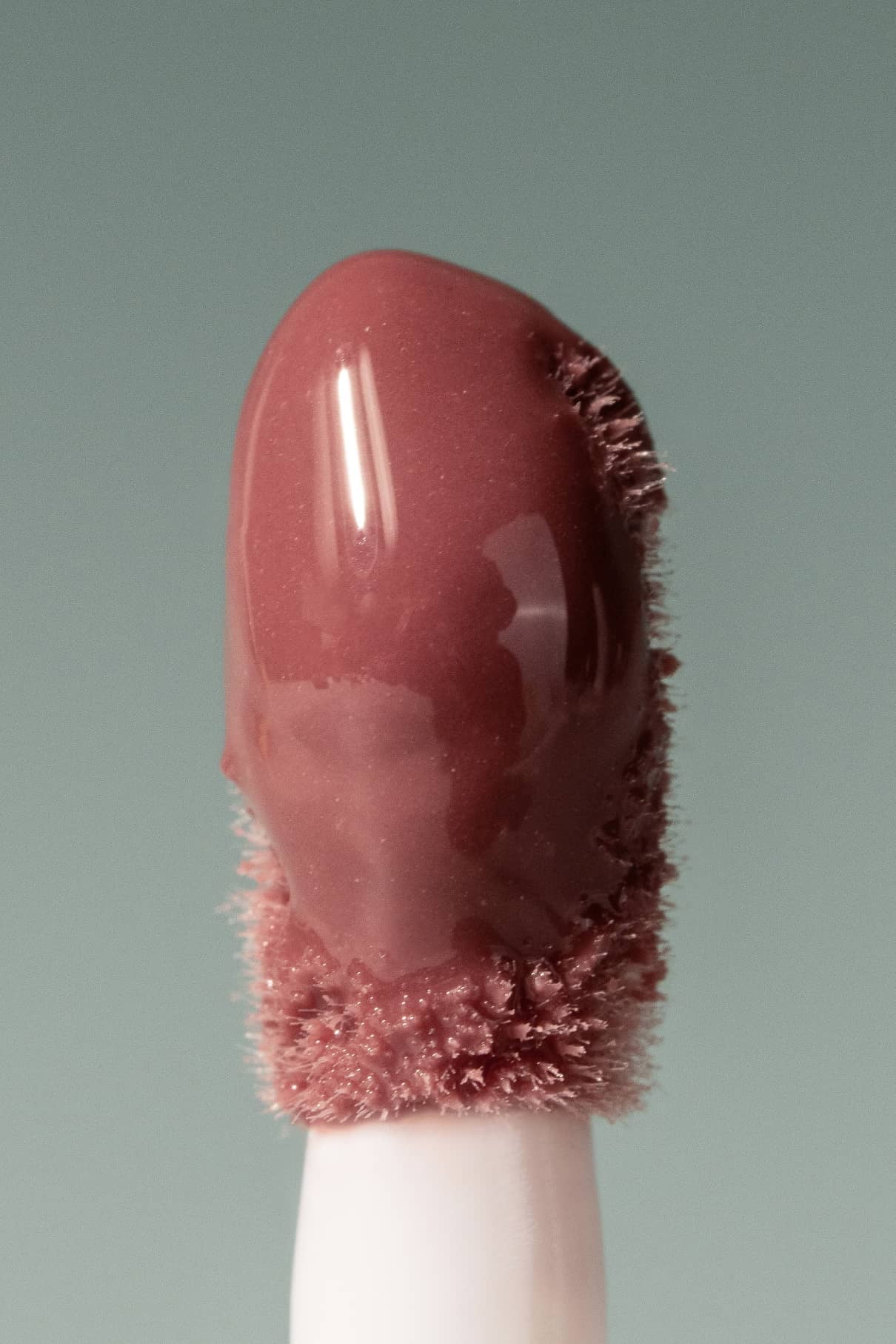 Nahaufnahme des Lip Glaze no. 01 Applikator mit mauvefarbenem Glanz an der Spitze, der sein hochglänzendes Finish vor einem schlichten Hintergrund hervorhebt.