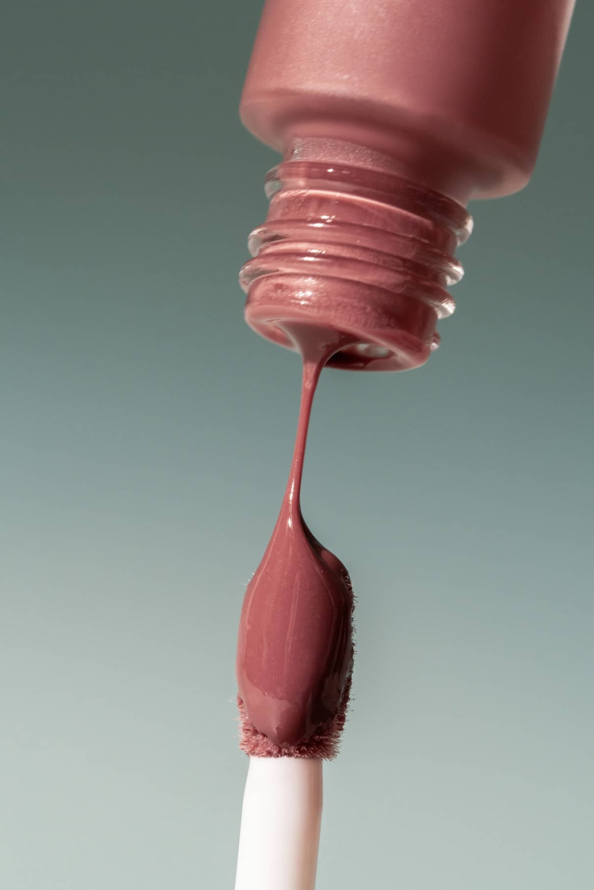 Nahaufnahme eines Pinsels, der in eine geöffnete Flasche Lip Glaze No. getaucht wird. 01 getaucht wird. Die Glasur bedeckt den Pinsel und bildet einen Tropfen, der sein hochglänzendes Finish für einen strahlenden Look zur Geltung bringt.