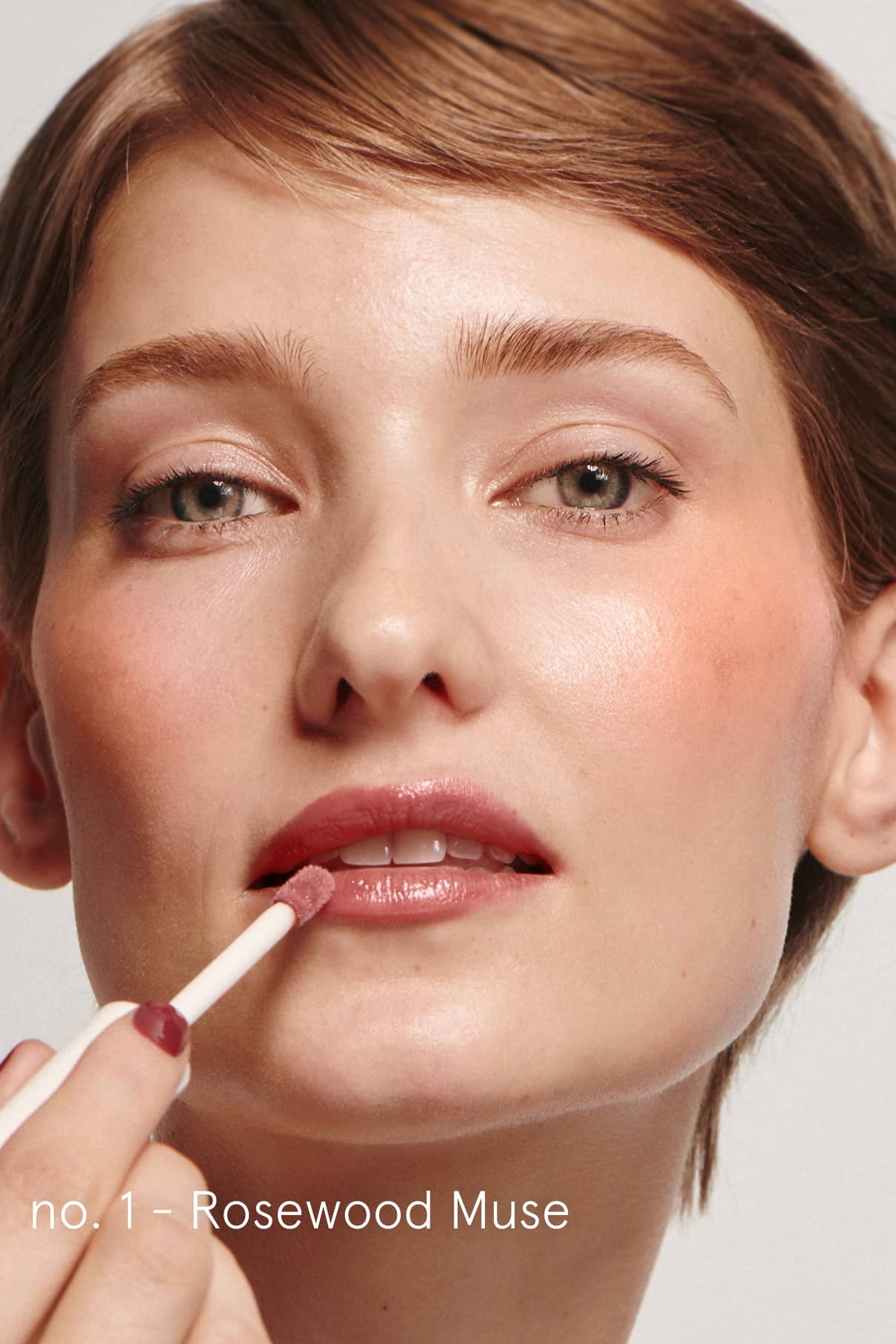 Eine Person mit kurzen braunen Haaren trägt das rosafarbene Lip Duo mit einem Applikator auf. Der Text lautet: no. 1 - Rosenholz Muse.