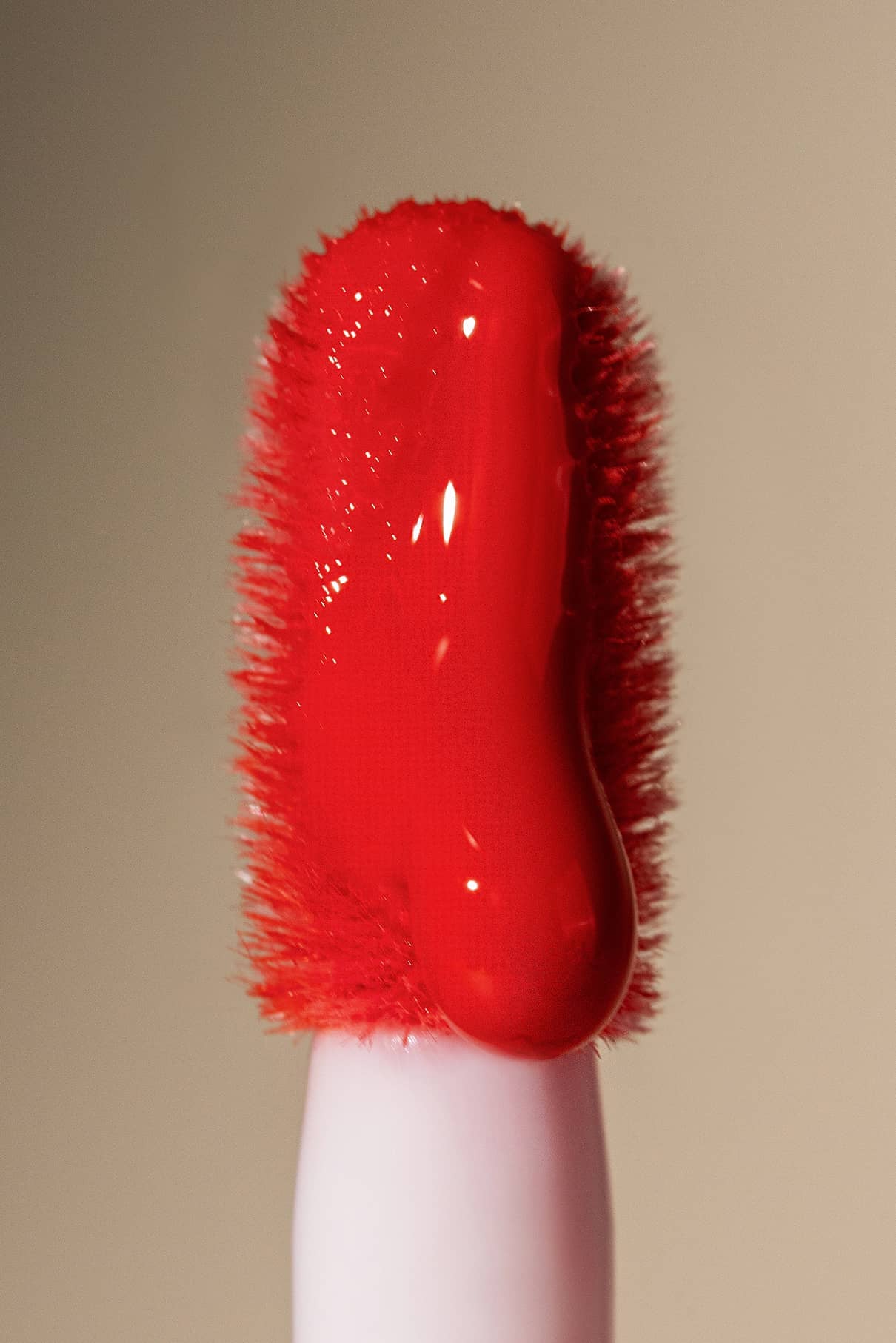 Eine Nahaufnahme des Lip Glaze no. 02 Applikatorstabs, der mit einer dicken Schicht des glänzenden roten Produkts überzogen ist, hebt sein hochglänzendes Finish vor einem neutralen Hintergrund hervor.