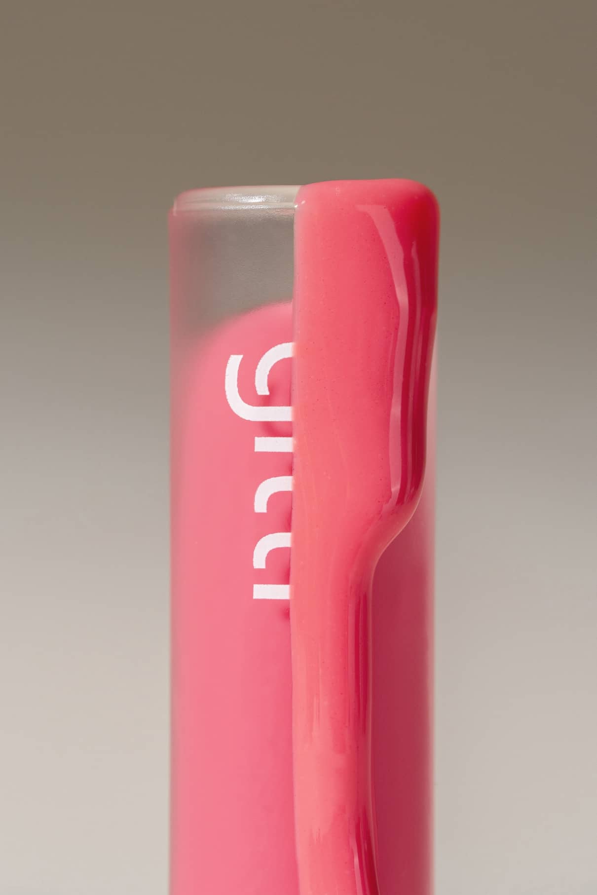 Nahaufnahme von Lip Glaze Nr. 03 mit Kunststoffclip und weißer Teilbeschriftung auf dem rosafarbenen Körper, mit hochglänzendem Finish, fotografiert vor einem unifarbenen Hintergrund.