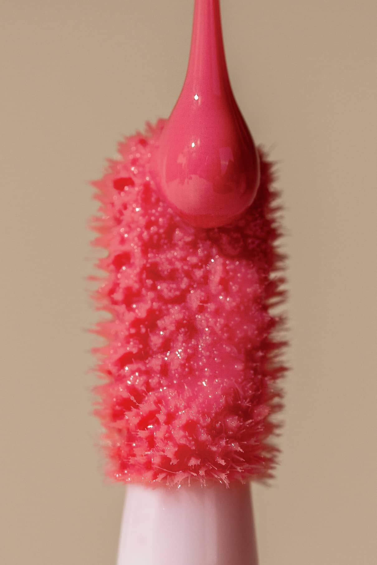 Nahaufnahme des Lip Glaze no. 03 Applikator mit einem rosafarbenen Tropfen an der Spitze, der das hochglänzende Finish vor einem beigen Hintergrund hervorhebt.