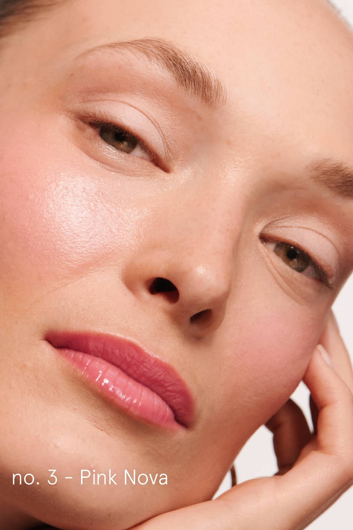 Nahaufnahme des Gesichts einer Person mit hellrosa Make-up und glänzenden Lippen, die das Lip Duo trägt und ihr Kinn auf die Hand stützt. Der Text lautet: no. 3 - Rosa Nova.