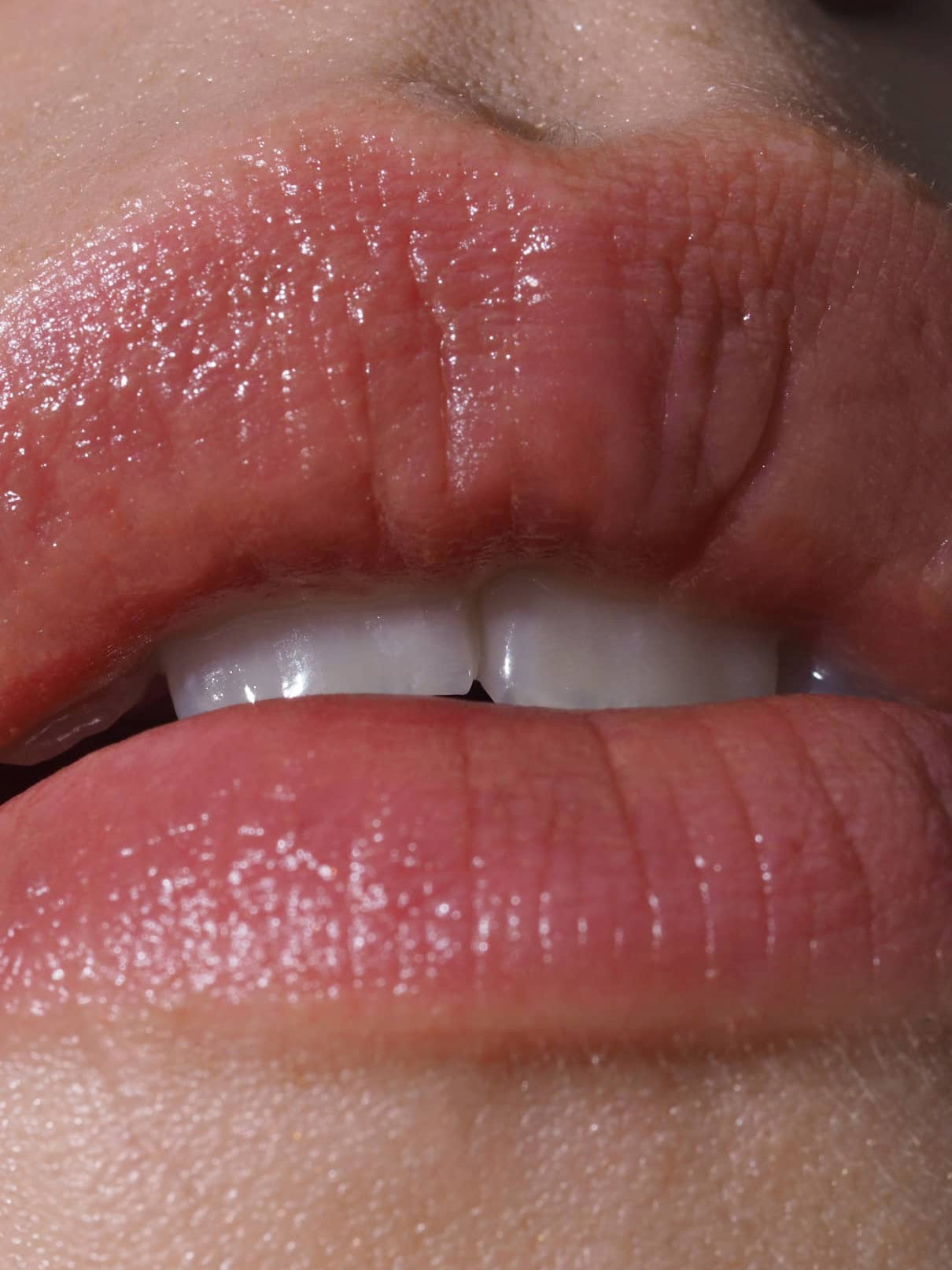 Nahaufnahme von Lippen und oberen Zähnen, die Lip Sync Refill Nr. 01, mit natürlichem Hautton mit rötlichem Unterton und Lichtreflexionen auf den feuchten Lippen.