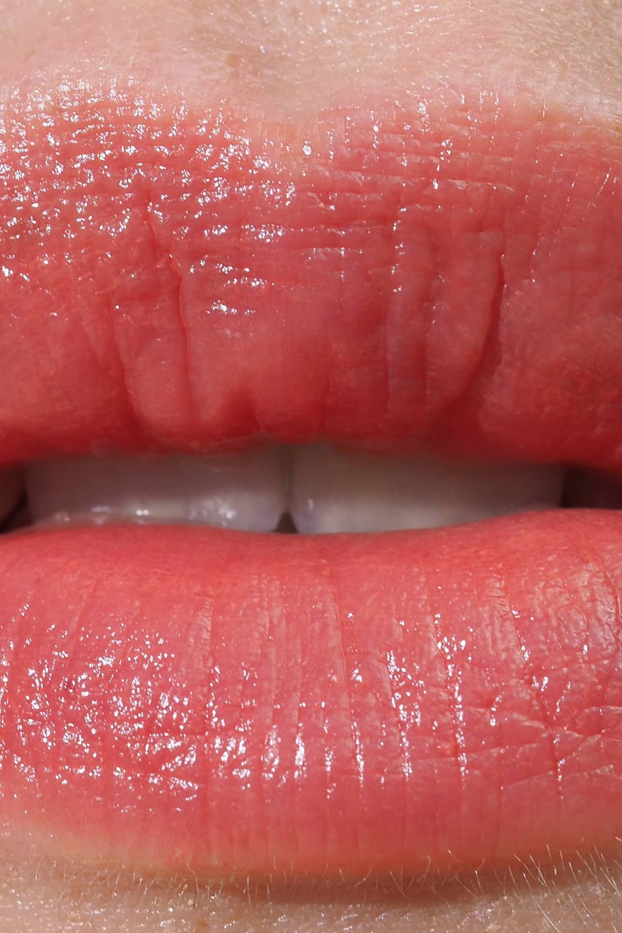 Nahaufnahme von Lippen in einem rosa Korallton, leicht glänzend und mit sichtbaren oberen Zähnen - perfekt für warme und neutrale Hauttypen. Getragen wird Lip Sync Refill no. 03.