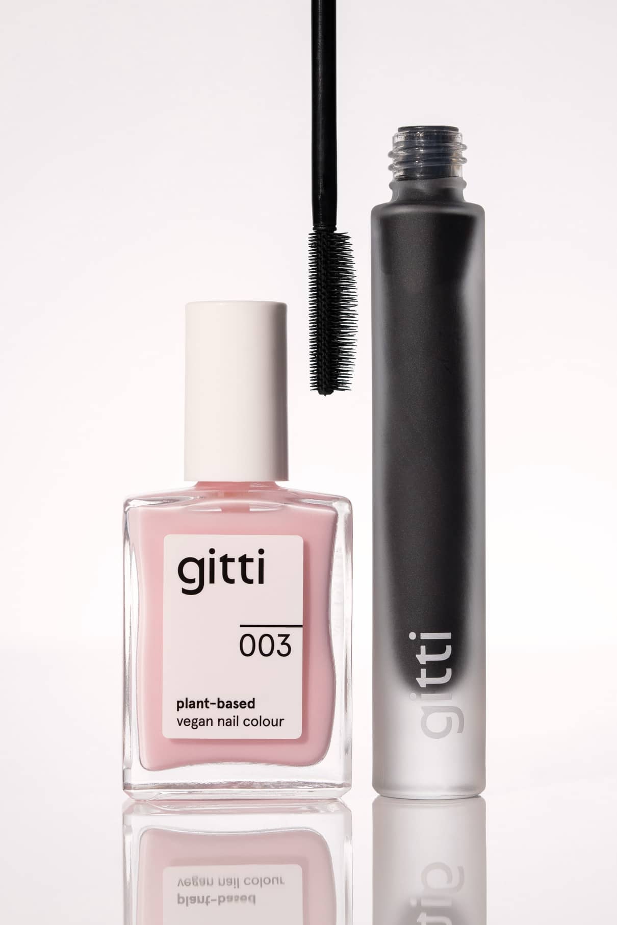 Das Colour Up Duo besteht aus einer pflanzenbasierten Nagelfarbe in pink gitti 003 und einer offenen schwarzen Mascara, die beide auf einer reflektierenden Oberfläche präsentiert werden.