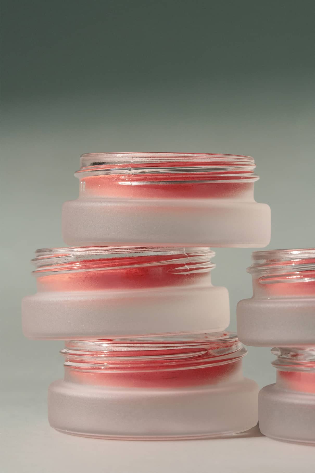 Vier mattierte Glastiegel von Velvet Cheeks no. 01 sind vor einem neutralen Hintergrund gestapelt und präsentieren das seidige, silikonfreie rosa Creme-Rouge im Inneren.