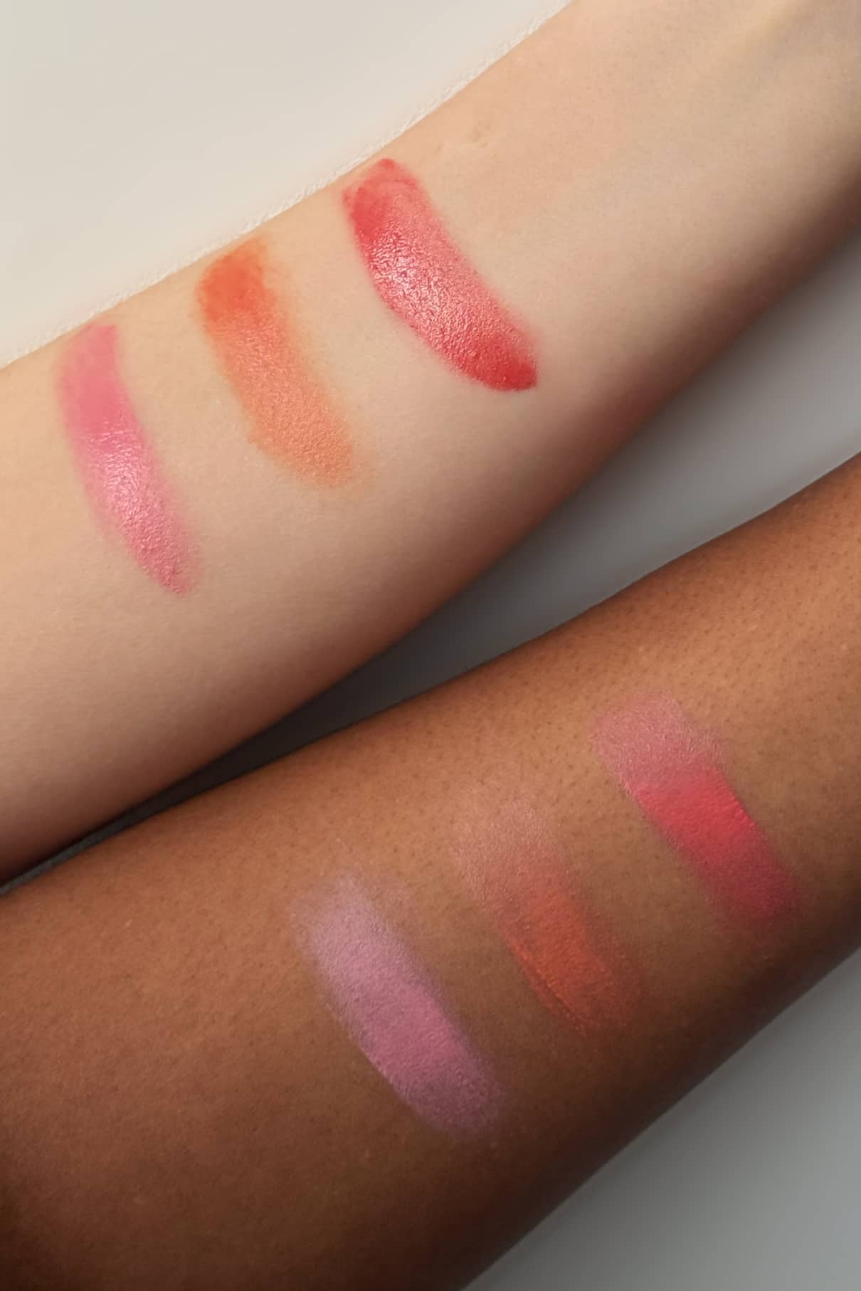 Auf zwei Unterarmen, einem hellen und einem dunklen, befinden sich jeweils vier Farbtupfer von Velvet Cheeks no. 01 Mousse-Blush in Pink, Orange und Beerenrot auf jedem Arm, um die Farbunterschiede zwischen den Hauttönen zu zeigen. Die silikonfreie Formel sorgt für ein natürliches Gefühl.