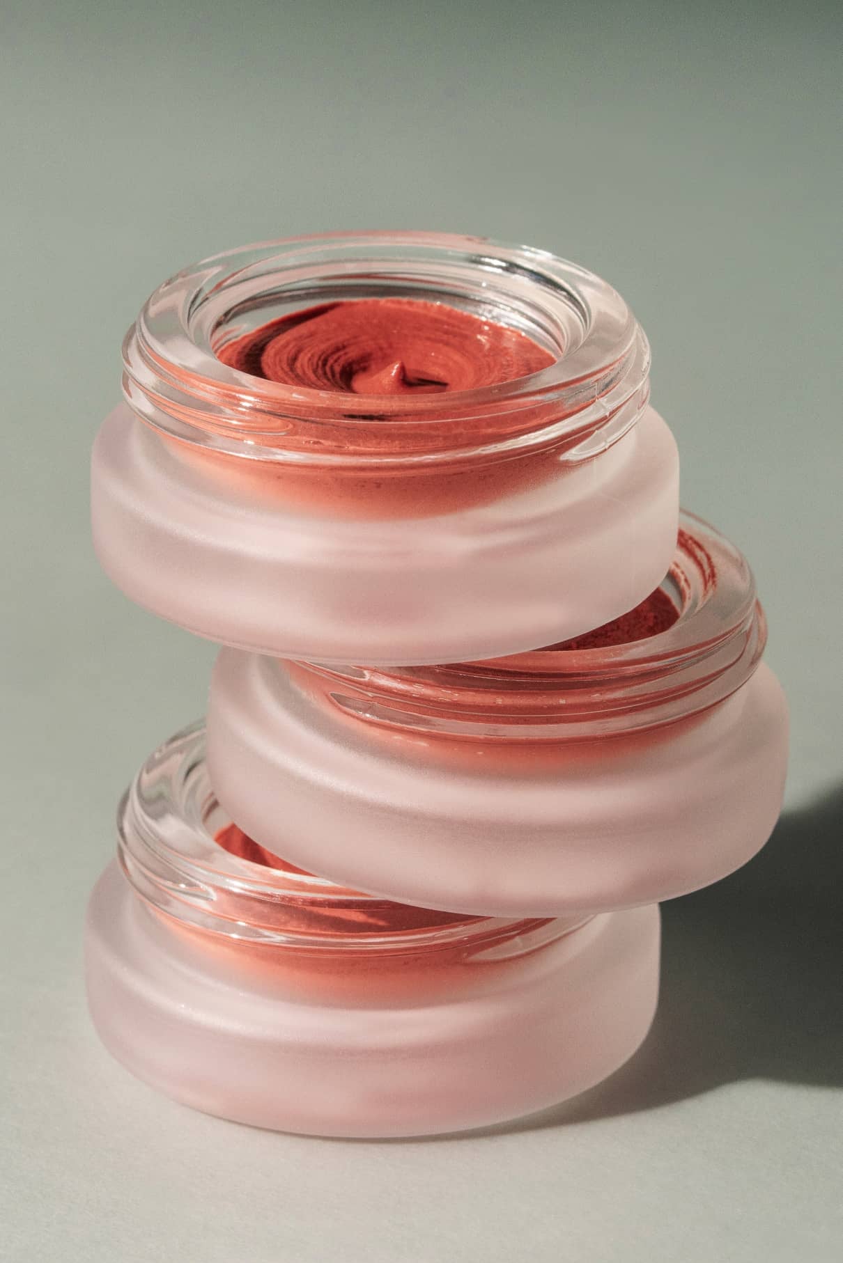 Drei mit rötlich-brauner Creme gefüllte Tiegel aus Milchglas sind ordentlich gestapelt und präsentieren das luxuriöse Lip & Cheek Duo vor einem neutralen Hintergrund.
