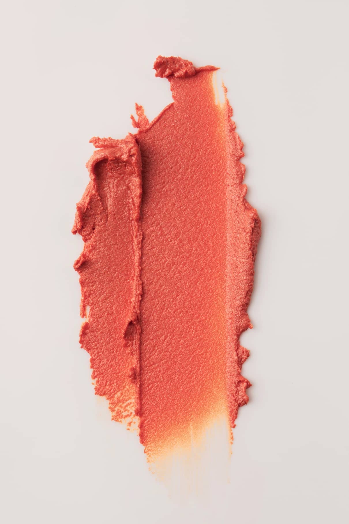 Eine Probe von Velvet Cheeks no. 02, ein leuchtendes und silikonfreies Mousse-Rouge in Korall-Orange, ist kunstvoll auf einen weißen Hintergrund aufgesprüht.