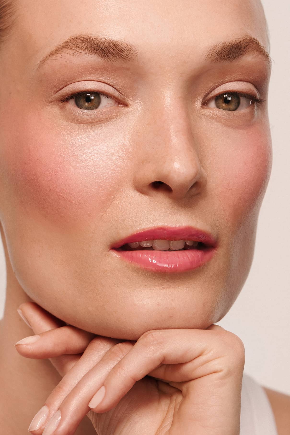 Eine Nahaufnahme einer Person mit hellem Hautton, natürlichem Make-up, Velvet Cheeks no. 03 mousse-blush auf den rosafarbenen Lippen und ordentlich gepflegten Augenbrauen, die ihr Kinn auf die Hand stützt.